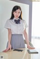 A woman in a white shirt and gray skirt posing at a desk.