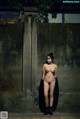A naked woman wearing a face mask standing in front of a wall.