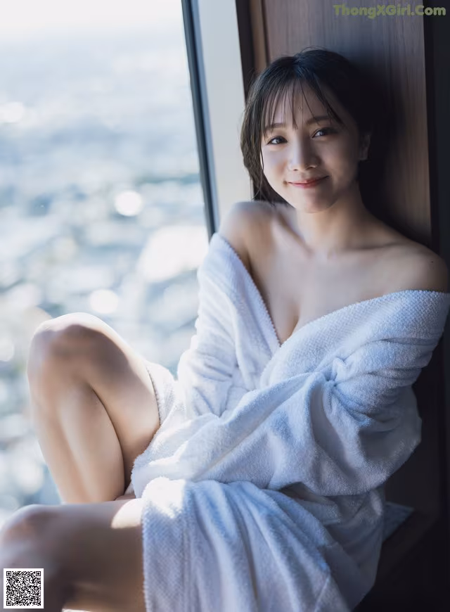 A woman in a white robe sitting by a window.
