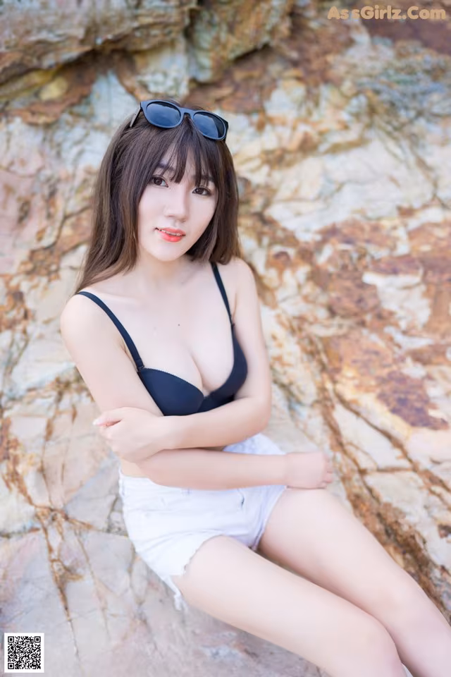 A woman in a black bra top and white shorts sitting on a rock.
