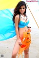 A woman in a blue bikini holding an umbrella on the beach.