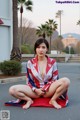 A woman in a red, white and blue kimono sitting on the ground.