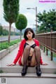 A woman in a red cardigan and black stockings sitting on some steps.