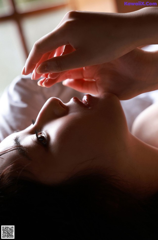 A woman laying on a bed with her eyes closed and her hands on her face.