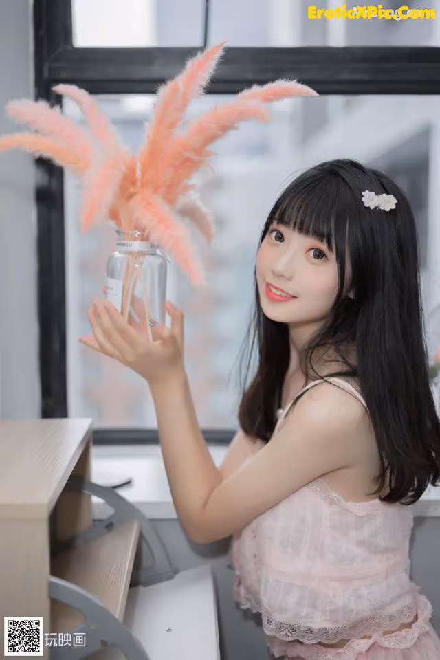 A woman in a pink dress holding a vase with pink feathers.