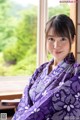 A woman in a purple kimono sitting in front of a window.