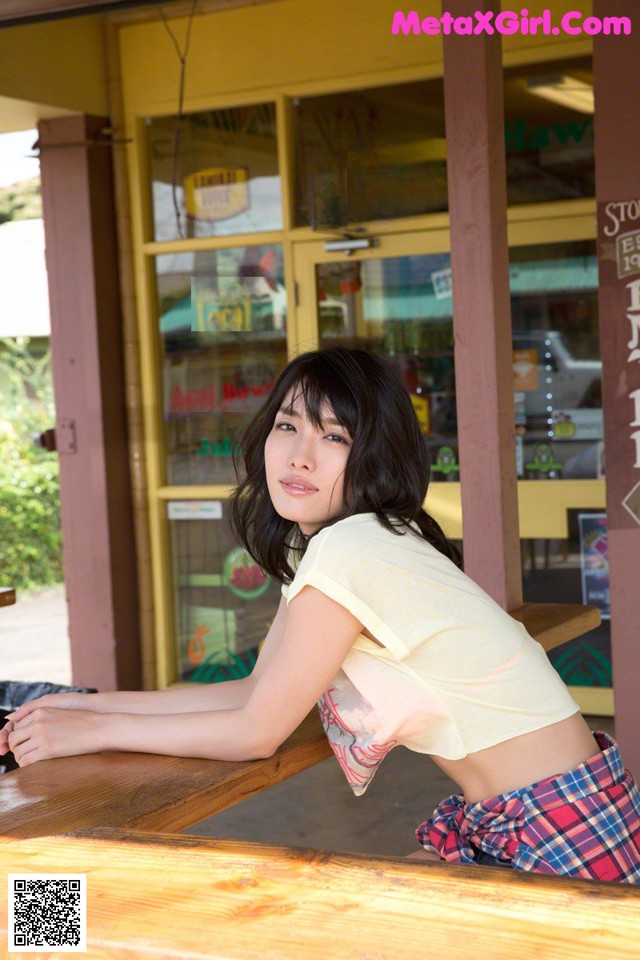 A woman leaning on a wooden table in front of a store.