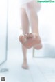 A woman standing in a bathroom with her feet in the shower.