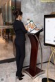 A woman standing in front of a menu on a stand.