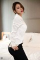 A woman in a white shirt and black pants posing on a bed.