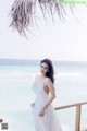 A woman in a white dress standing on a balcony overlooking the ocean.