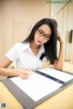 A woman sitting at a desk writing on a clipboard.