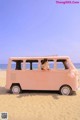 A woman sitting in the back of a pink van on the beach.