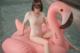 A woman sitting on an inflatable flamingo in a pool.