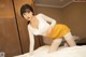 A woman in a white top and yellow skirt posing on a bed.