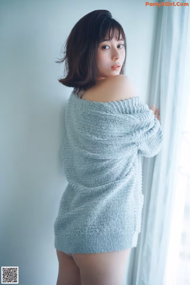 A woman in a blue sweater leaning against a window.
