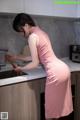 A woman in a pink dress standing in a kitchen.