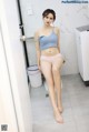 A woman in a blue top and pink panties sitting on a toilet.